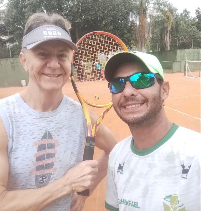 Rafael ao lado de um aluno que segura a raquete numa quadra de saibro